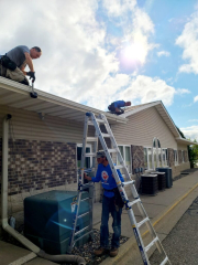 Three workers installing seamless gutters on a residential home, using ladders and tools for precise installation