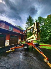 Two workers installing seamless gutters on a two-story cedar home using a towable boom lift for safe and precise placement