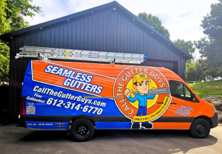 Brightly wrapped work van for 'Call The Gutter Guys' with ladders on top, advertising seamless gutter services and contact information